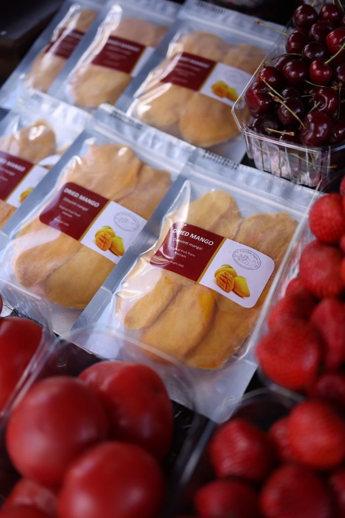 Packaged dried mangoes alongside fresh cherries and tomatoes in a market display.