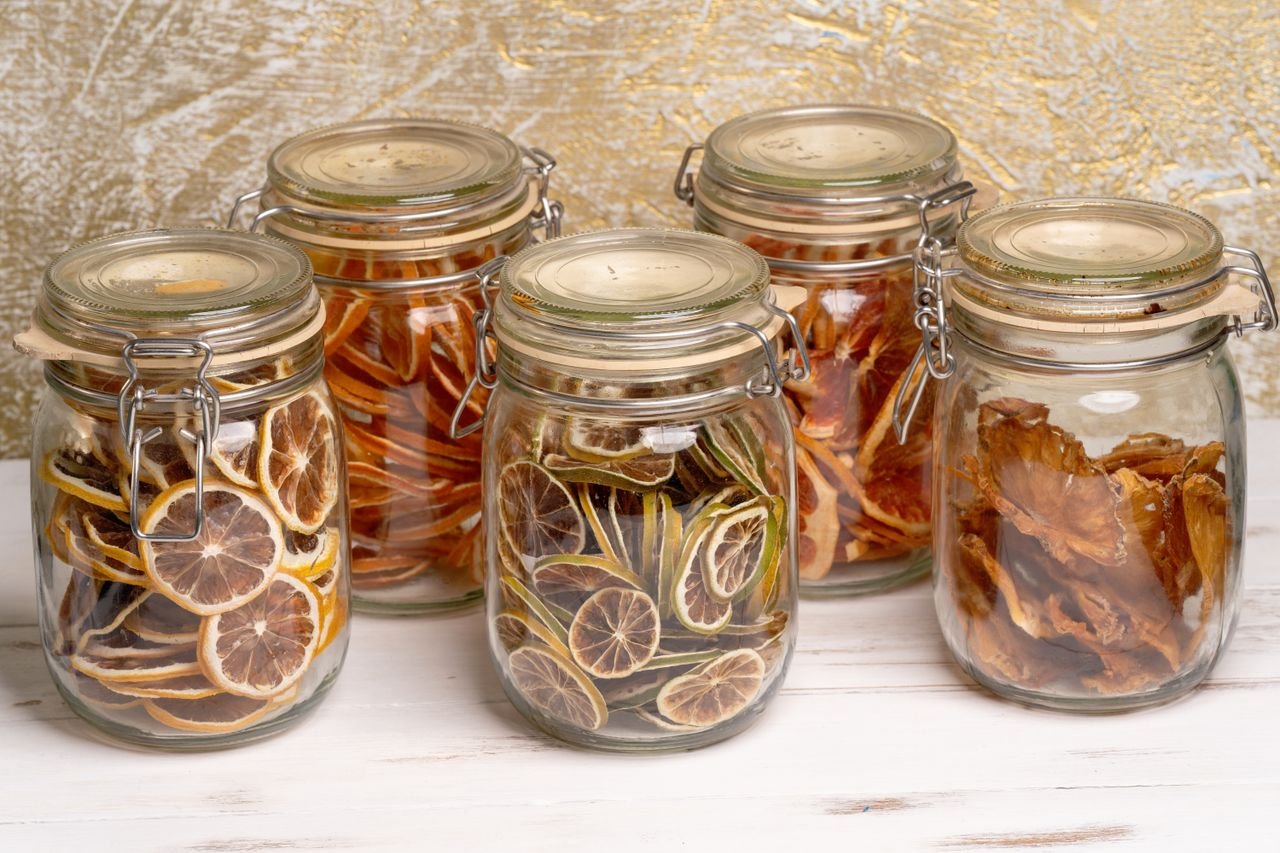 Glass jars filled with preserved citrus and tropical fruit slices on a white table.